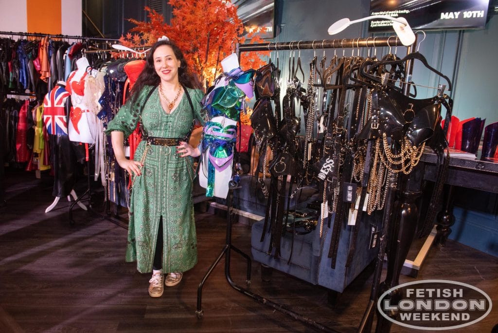 An exhibitor at her stand surrounded by racks of fetish fashion