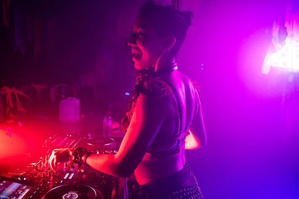 Mattana laughing over her shoulder while mixing, lit in deep pink and purple